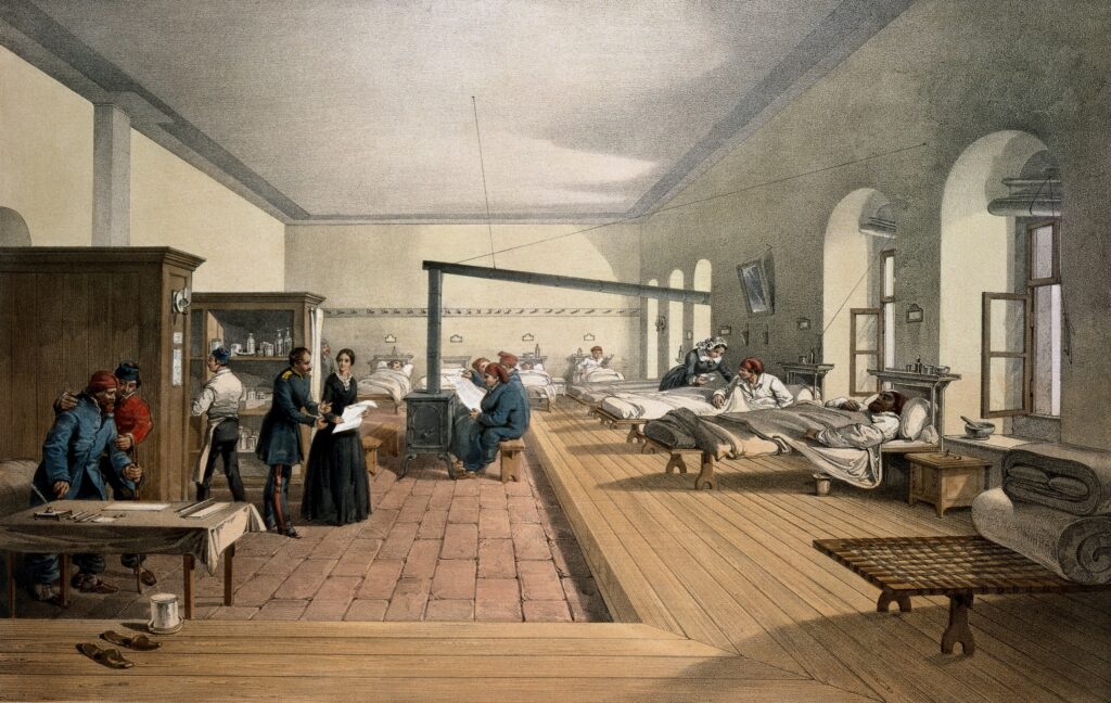 Lithograph of a ward at Scutari military hospital during the Crimean War. The lithograph shows Florence Nightingale consulting with a military officer while a group patients seek warmth from a wood burner in the centre of the room. Other patients are lying down on beds positioned around the outside of the ward. 