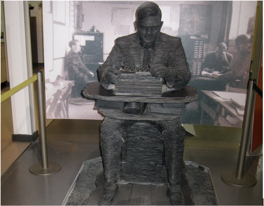 Iron statue of Alan Turing, a man sitting at a desk using an enigma machine