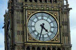 A zoomed in color photograph of the clock face of big ben. The building is in the style of neo Victorian gothic. There are roman numerals with golden accents on the face.